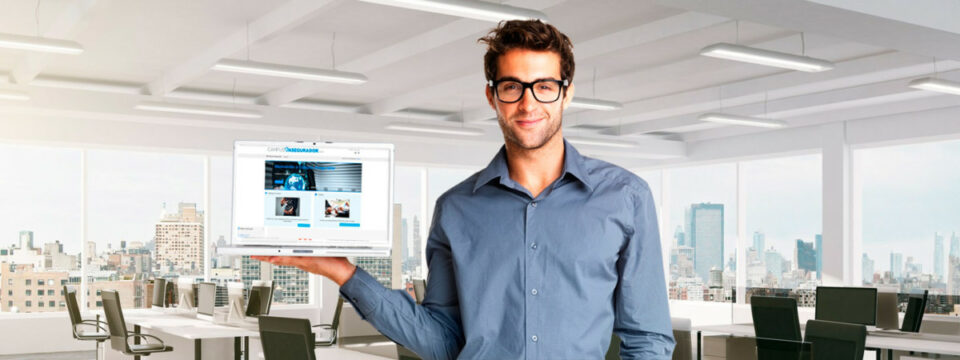 Profesional con gafas sosteniendo portátil con portal Campus Asegurador en oficina diáfana con vistas urbanas.