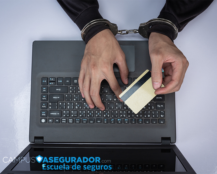 Manos esposadas operando laptop y tarjeta de crédito, representando fraude financiero y delitos informáticos.