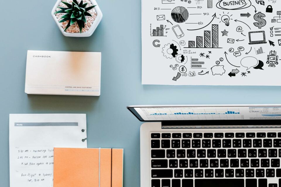 Laptop, cashbook, suculenta y gráficos de estrategia empresarial sobre escritorio azul grisáceo, composición flat lay.