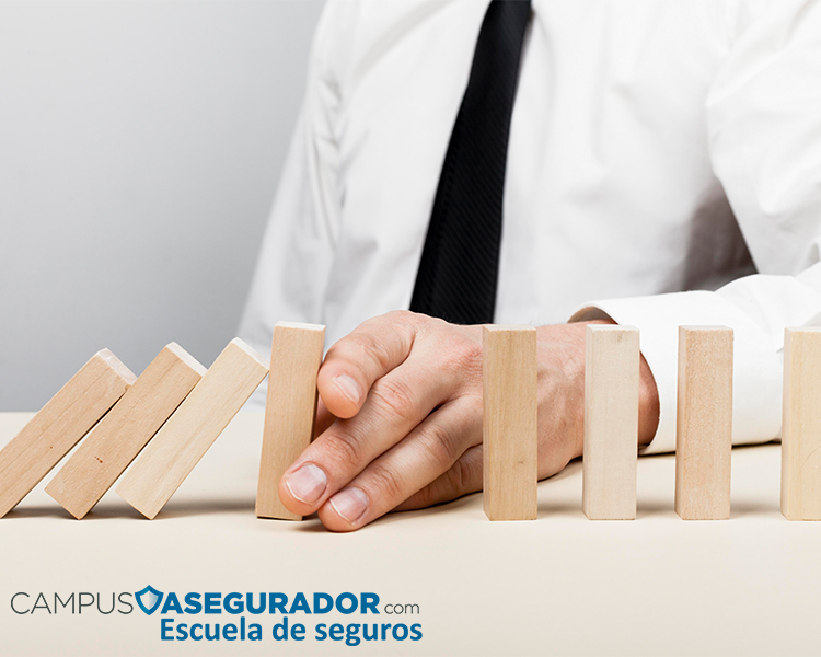 Mano deteniendo efecto dominó de bloques de madera, simbolizando prevención y gestión de riesgos en el sector seguros.