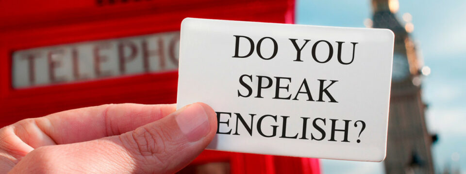 Mano sosteniendo tarjeta blanca con texto Do you speak English frente a cabina telefónica roja y Elizabeth Tower en Londres.