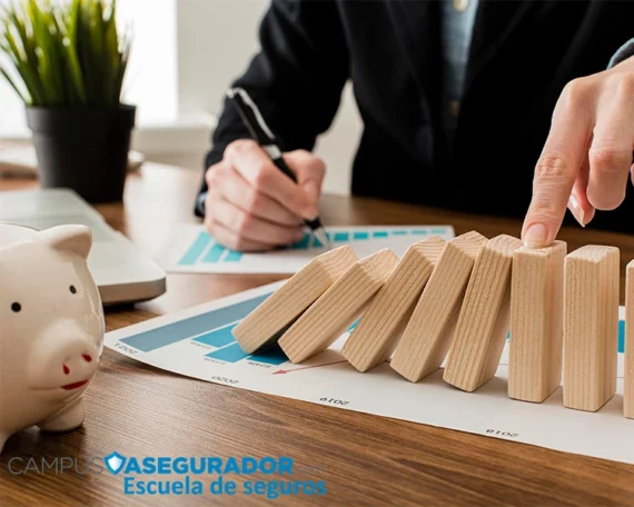Mano deteniendo caída de domino sobre gráficos financieros junto a hucha y logotipo de Campus Asegurador.