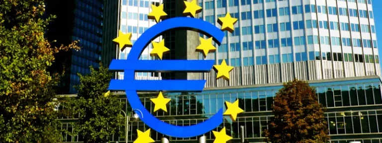 Escultura azul del símbolo euro con estrellas amarillas ante rascacielos de cristal en el distrito financiero de Frankfurt.