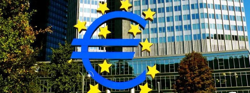 Escultura azul del símbolo euro con estrellas amarillas ante rascacielos de cristal en el distrito financiero de Frankfurt.