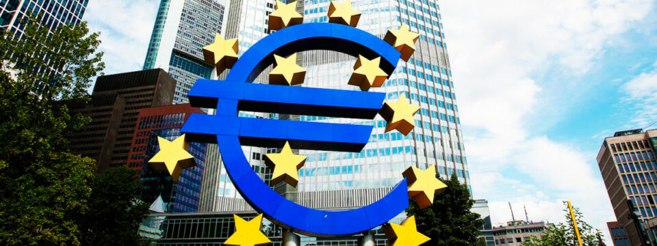 Escultura azul del símbolo euro rodeada de estrellas amarillas frente a rascacielos en Frankfurt.