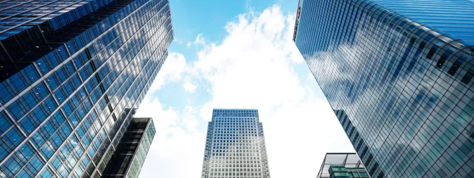 Perspectiva contrapicada de rascacielos financieros en Canary Wharf, Londres, con fachadas de vidrio y acero reflectante.