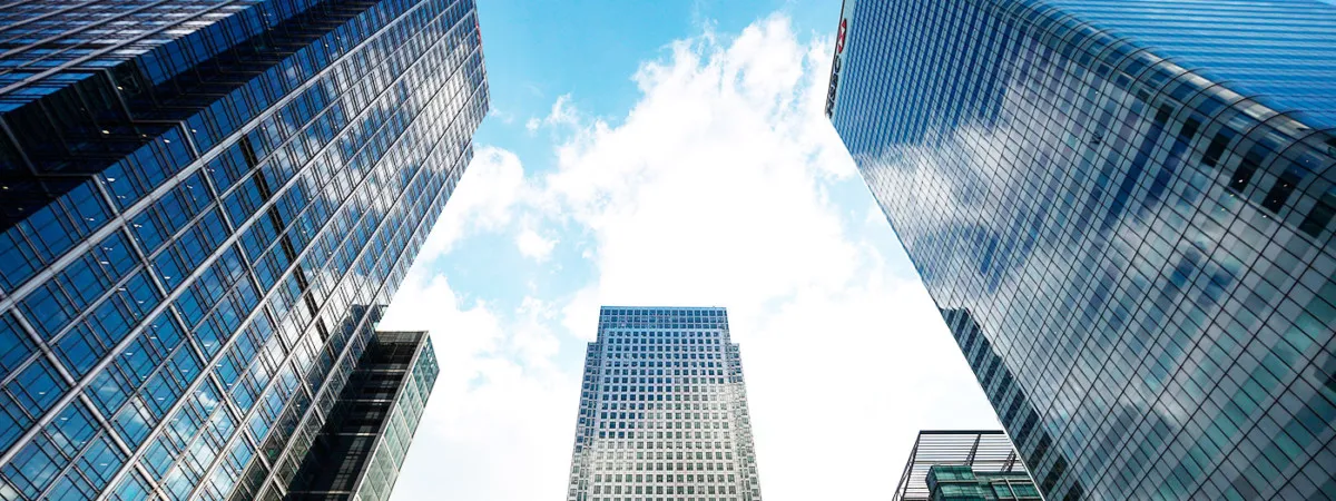 Perspectiva contrapicada de rascacielos financieros en Canary Wharf, Londres, con fachadas de vidrio y acero reflectante.