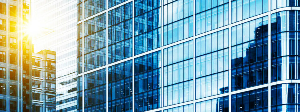 Fachada de rascacielos con paneles de vidrio azul y reflejos solares en un entorno urbano de arquitectura moderna.