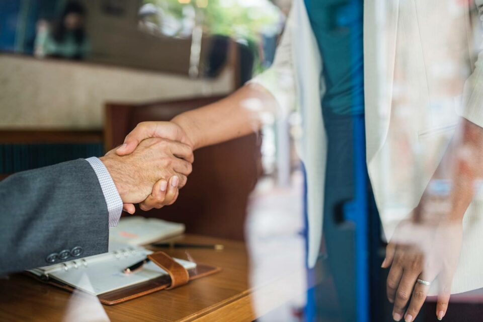 Primer plano de profesionales estrechando sus manos sobre una mesa de oficina tras cerrar un acuerdo corporativo.
