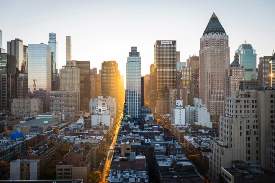 Panorámica de Manhattan al atardecer con luz solar en una avenida central entre rascacielos y el edificio Allianz.