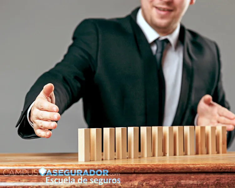 Profesional deteniendo una hilera de bloques de madera para evitar el efecto dominó. Marca Campus Asegurador visible.