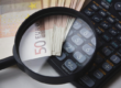 Lupa sobre billetes de 50 euros y calculadora científica en contexto de auditoría, contabilidad y análisis financiero.
