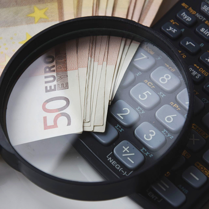 Lupa sobre billetes de 50 euros y calculadora científica en contexto de auditoría, contabilidad y análisis financiero.
