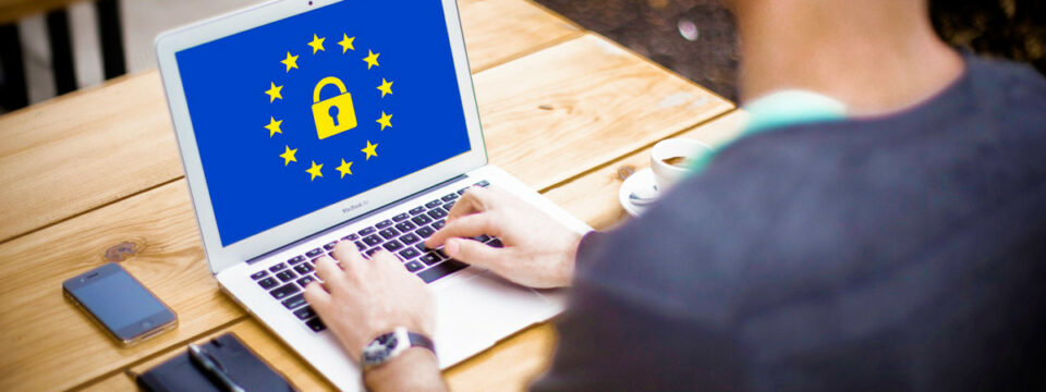 MacBook Air con bandera de la UE y candado amarillo, simbolizando cumplimiento GDPR y ciberseguridad en entorno laboral.