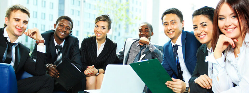 Grupo multicultural de profesionales de negocios sonriendo en reunión corporativa con laptops y carpetas de trabajo.