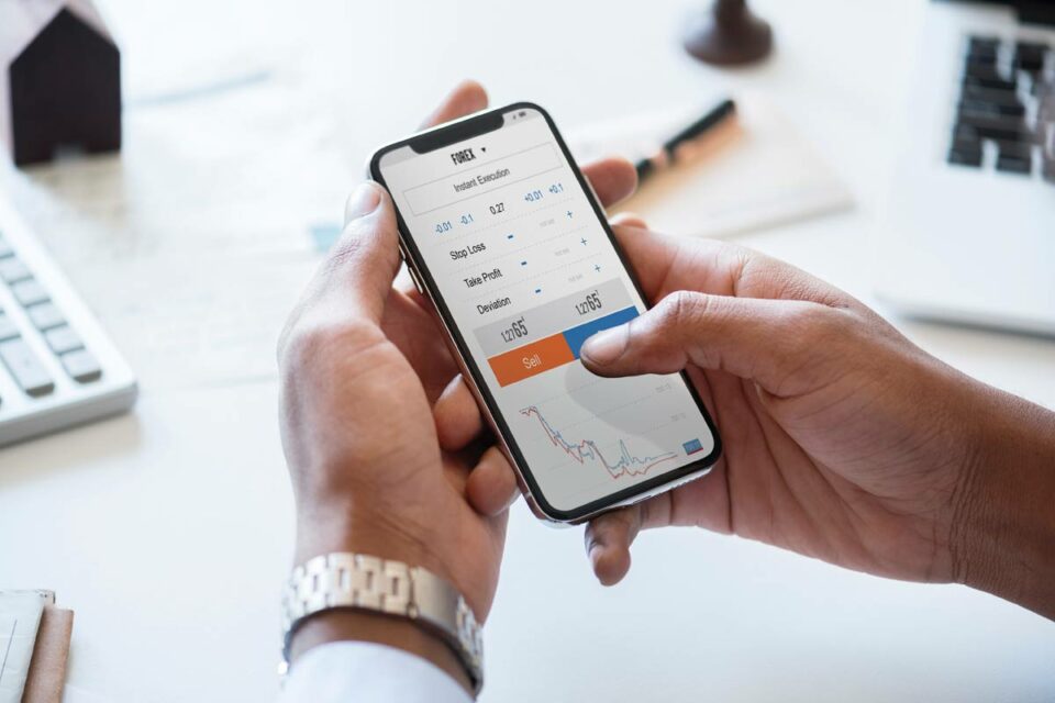 Persona usando app móvil de trading Forex para analizar gráficos financieros y ejecutar órdenes de mercado.
