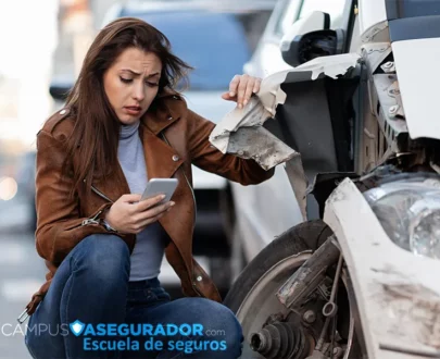 Mujer angustiada usa móvil junto a coche blanco con graves daños estructurales tras colisión. Logo Campus Asegurador.