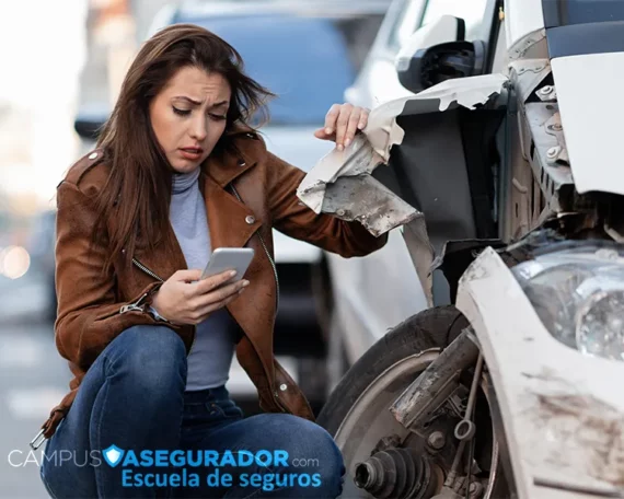 Mujer angustiada usa móvil junto a coche blanco con graves daños estructurales tras colisión. Logo Campus Asegurador.