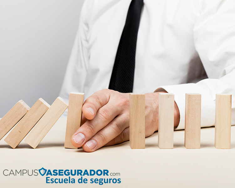 Mano detiene efecto dominó de bloques madera simbolizando gestión riesgos y protección financiera en sector asegurador.