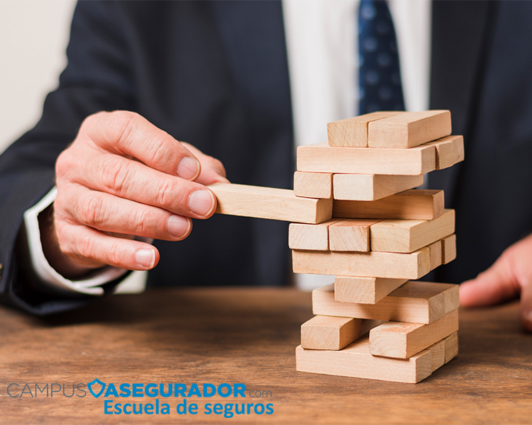 Ejecutivo manipulando torre bloques madera simbolizando gestión riesgos financieros con logotipo Campus Asegurador.