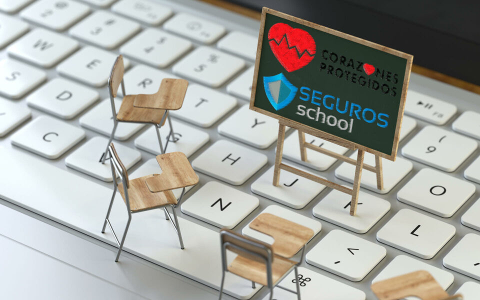 Pupitres y pizarra de Seguros School y Corazones Protegidos sobre teclado de laptop blanco. Concepto educación digital.