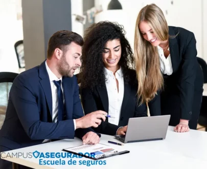 Tres profesionales colaborando con laptop y gráficos impresos en Campus Asegurador, escuela técnica de seguros.