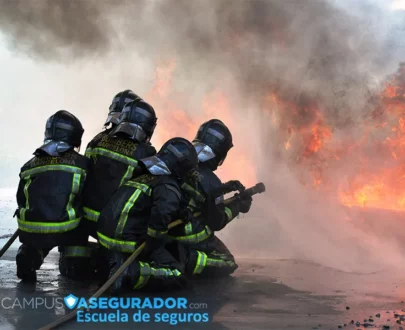Bomberos de Barcelona con equipo de protección operando manguera de alta presión frente a llamas y humo denso.