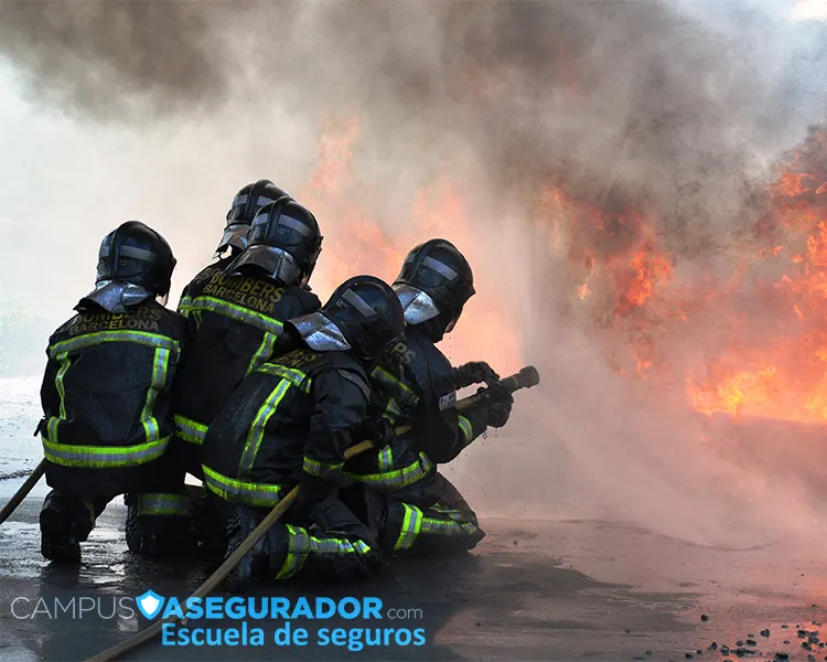 Bomberos de Barcelona con equipo de protección operando manguera de alta presión frente a llamas y humo denso.