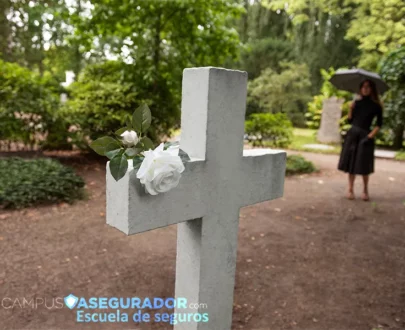 Cruz de piedra con rosas blancas en cementerio, mujer de luto con paraguas al fondo. Logo Campus Asegurador.