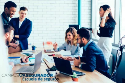 Profesionales en formación de seguros colaborando en oficina moderna con portátiles para Campus Asegurador.