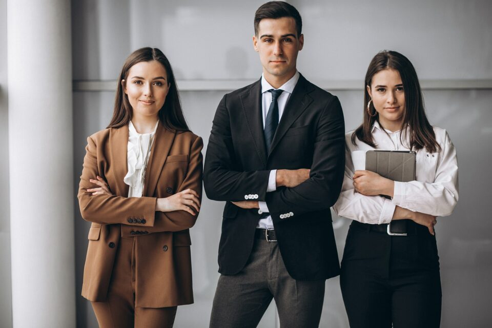 Tres profesionales de negocios posando con traje y tablet en entorno corporativo minimalista.