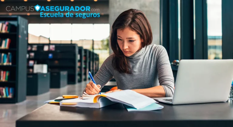 Estudiante redacta apuntes junto a ordenador y libros en Escuela de Seguros Campus Asegurador.