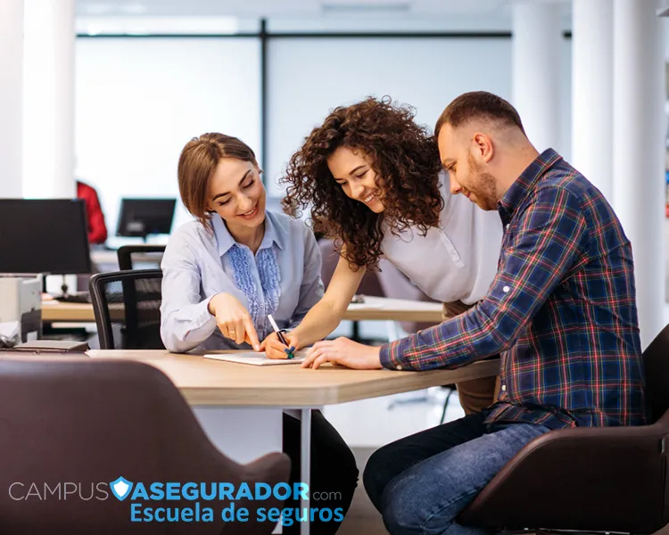 Tres personas colaborando y revisando documentos en la Escuela de Seguros Campus Asegurador.