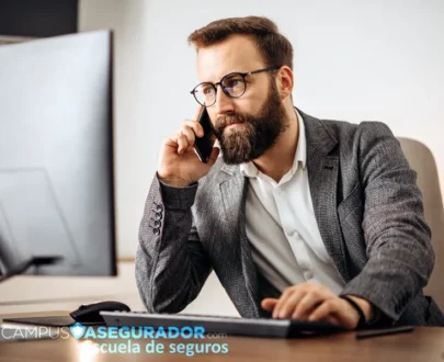Asesor de seguros atendiendo llamada telefónica frente a monitor en entorno corporativo de Campus Asegurador.