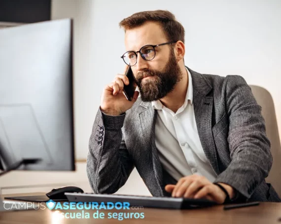 Asesor de seguros atendiendo llamada telefónica frente a monitor en entorno corporativo de Campus Asegurador.