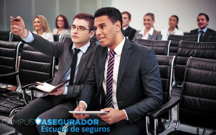 Alumnos en formación técnica de seguros de Campus Asegurador con dispositivos digitales y material de estudio en aula.