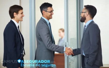 Tres profesionales de negocios estrechan manos en oficina, logo de Campus Asegurador, escuela de seguros al frente.