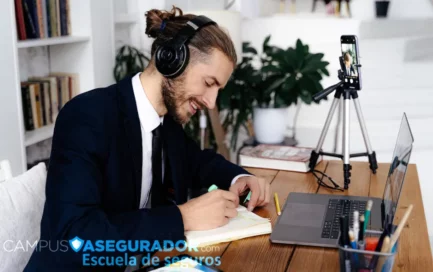Profesional en traje tomando notas durante formación online de seguros con portátil y smartphone en Campus Asegurador.