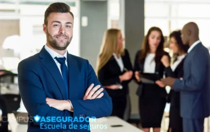 Profesional sonriente con traje azul y brazos cruzados frente a equipo de trabajo en oficina de Campus Asegurador.