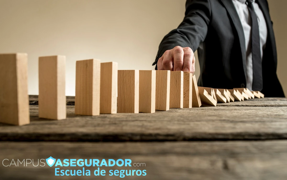 Mano deteniendo caída bloques madera efecto dominó para ilustrar prevención de riesgos y seguros de Campus Asegurador.
