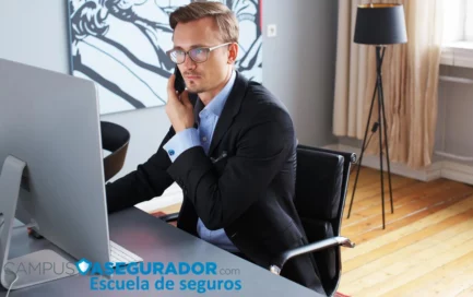 Profesional con traje usando smartphone frente a monitor en oficina de Escuela de seguros Campus Asegurador.
