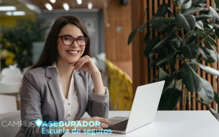 Estudiante de seguros con portátil y gafas rojas en oficina moderna para Campus Asegurador Escuela de seguros.