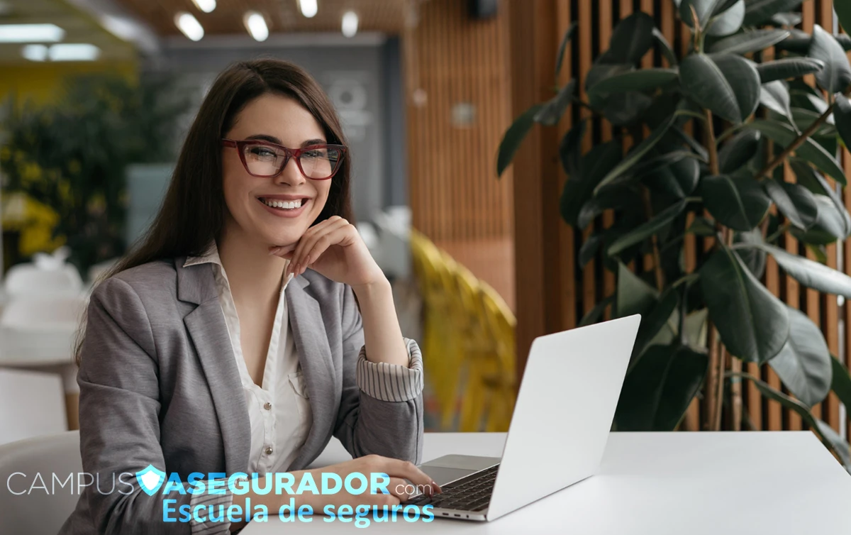 Estudiante de seguros con portátil y gafas rojas en oficina moderna para Campus Asegurador Escuela de seguros.