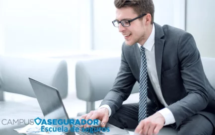 Hombre en traje usando laptop con logotipo de Campus Asegurador Escuela de seguros en ambiente de oficina iluminado.
