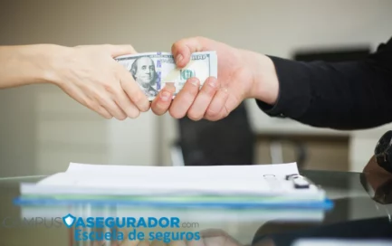 Manos estrechándose sujetando billetes de cien dólares sobre un contrato en oficina de Campus Asegurador.