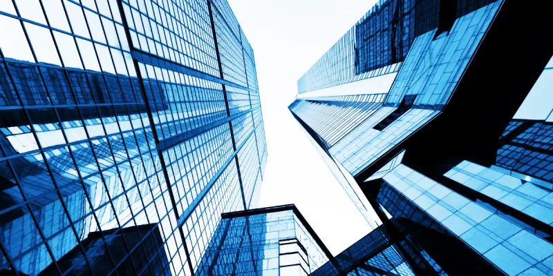 Perspectiva contrapicada de rascacielos modernos con fachadas de cristal azul en un distrito financiero bajo cielo claro.