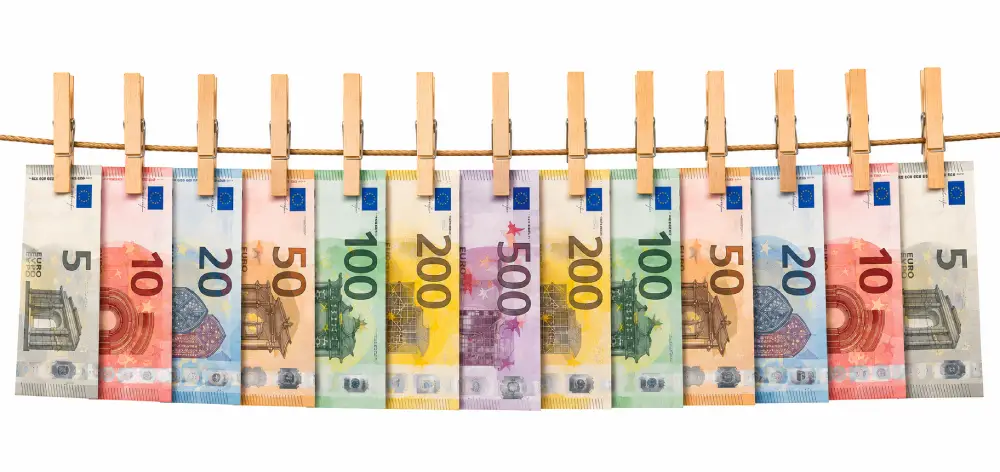 Billetes de euro de varias denominaciones sujetos con pinzas de madera en un tendedero sobre fondo blanco minimalista.