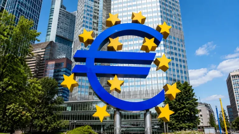 Símbolo del Euro en Frankfurt: Icono de la Economía Escultura azul del símbolo euro rodeada de estrellas amarillas frente a rascacielos en Frankfurt.