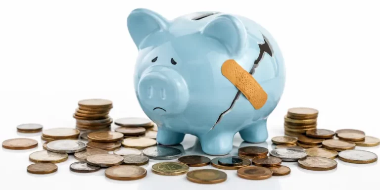 Impacto de la Crisis en el Ahorro y Finanzas Personales Hucha de cerdo azul agrietada con un apósito adhesivo rodeada de monedas sobre fondo blanco para ahorro y finanzas.