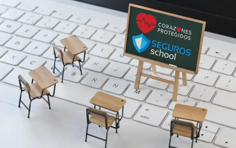 Formación Digital en Seguros School Corazones Protegidos Pupitres y pizarra de Seguros School y Corazones Protegidos sobre teclado de laptop blanco. Concepto educación digital.